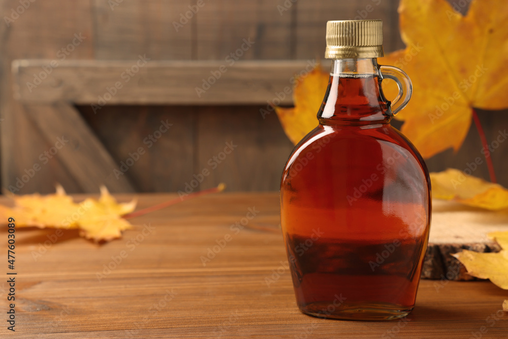Wall mural bottle of tasty maple syrup and dry leaves on wooden table, space for text
