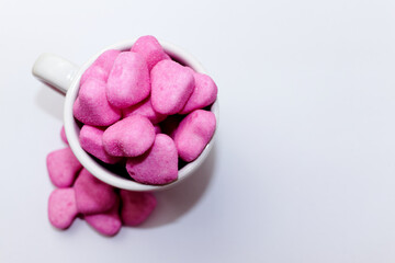 Heap of pink heart-shaped candies in a white cup on a white background