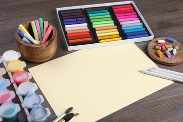 Blank sheet of paper, colorful chalk pastels and other drawing tools on wooden table. Modern...