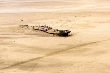 A horizontal aerial shot from an aeroplane of a sand covered shipwreck, Namibian desert landscape 