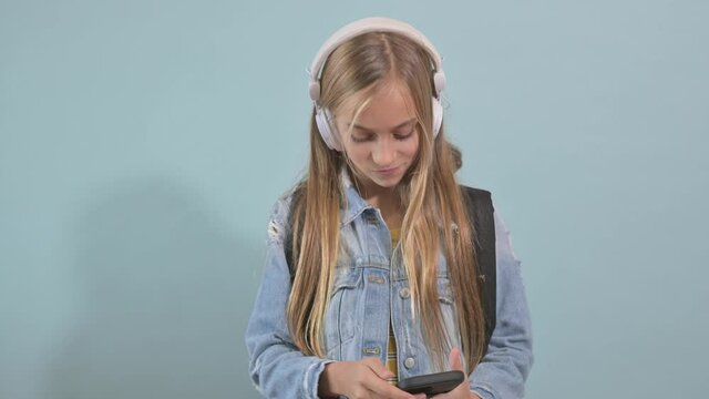 Young blonde girl with blue eyes listening to music with headphones.