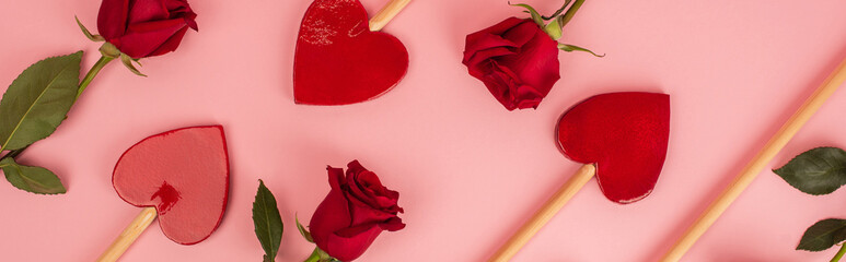 flat lay of heart-shaped lollipops near red roses on pink banner.
