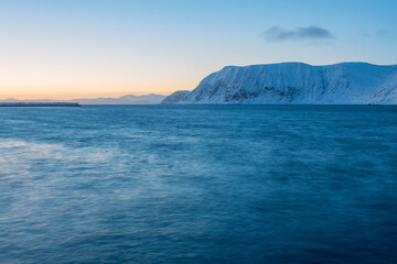 A tranquil horizontal seascape in winter with snow covered mountains in the background, after sunset, Norway