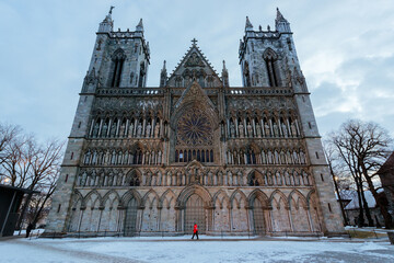 A moody wide angle horizontal photograph of the Nidaros Cathedral in Norway in the early morning, with a cloudy sky as the background