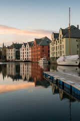 A vertical sunset photograph of beautiful buildings reflecting off the water, with a blue sky with clouds in the background, taken in Aalesund, Norway