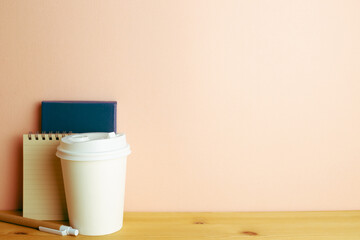 Notebook, pen, paper coffee cup on wooden desk. pink wall background. workspace