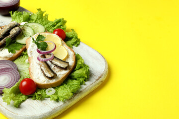 Fototapeta na wymiar Board with sandwiches with sprats on yellow background