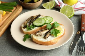 Concept of tasty snack with sandwiches with sprats on gray textured background