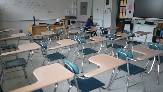 Lone student works at her desk in a darkened empty school classroom.