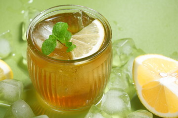 Iced tea with lemon slices and mint on green background