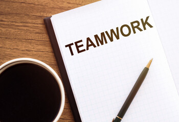TEAMWORK word in notebook on the wooden desk next to glasses, a cup of coffee and a pencil