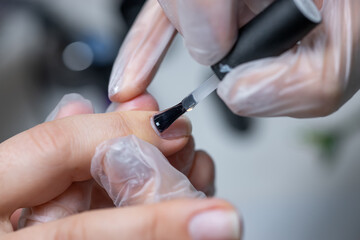 the master of the nail service makes a manicure to apply the gel with a brush on the treated nail