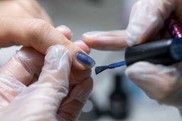 the nail service master makes a manicure by distributing blue gel polish with a nail brush on the nail surface
