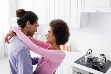 Side view of african american woman embracing young man in kitchen.