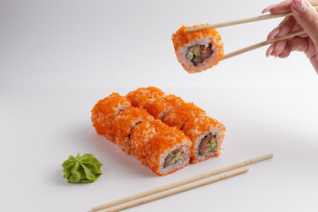a hand and Chinese chopsticks holds a roll over other sushi, a portion of Asian food, rolls