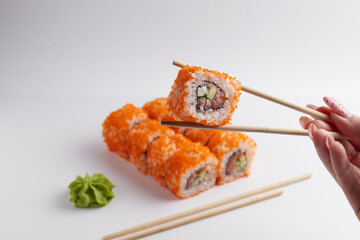 a hand and Chinese chopsticks holds a roll over other sushi, a portion of Asian food, rolls