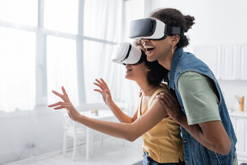 Positive african american couple in vr headsets gaming at home.