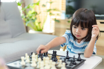 Little sibling girl playing chess at home.