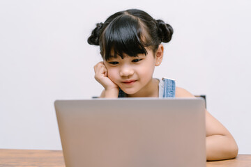 Smiling little Asian girl learning internet online class and do homework studying knowledge with...