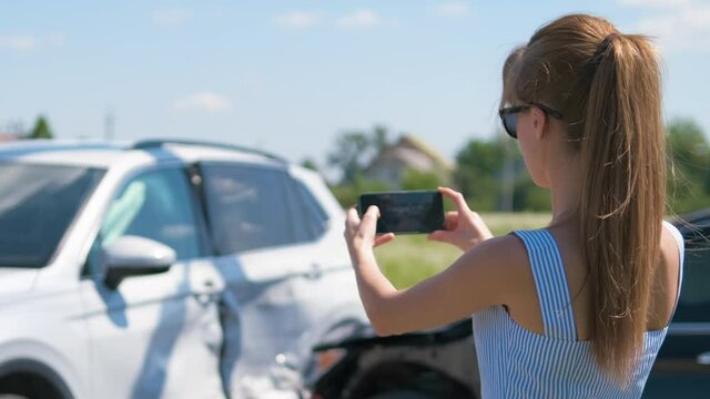Stressed woman driver taking photo on mobile phone camera after vehicle collision on street side for emergency service after car accident. Road safety and insurance concept