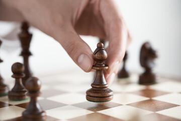 Female fingers hold a chess piece officer. Wooden chess piece in the hands of a player making a move on a wooden chessboard.

