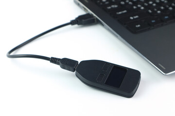 black hardware wallet for buying , selling and protecting the crypto currency from hackers is connected with the notebook computer on the white table during playing nft game defi
