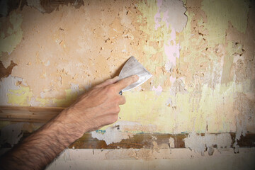 Male hand removing old wallpaper from the wall.