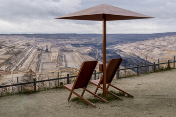 two empty deck chairs with an umbrella made of metal in front of open pit mining of hambach terra...