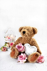 Cute teddy bear with roses and a heart sitting on white background