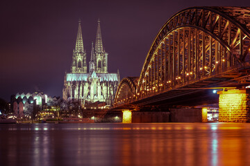Obraz premium The illuminated Cologne Cathedral on the Rhine and the Hohenzollern Bridge in Cologne at night with purple sky.
