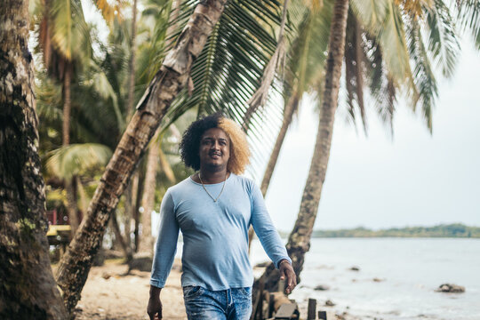 Positive black man walking between palms on beach