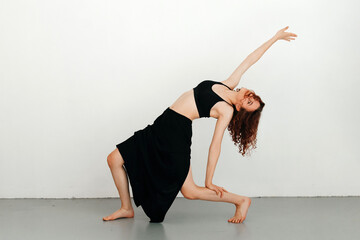 Young redhead woman dancer performing dance move, leaning on her led, stretching her arm up, skirt...