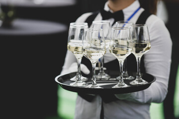 Shallow depth of field (selective focus) details with a waiter walking around and offering glasses of wine to the guests of an event.