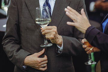 Details with a man and a woman interacting at a classy event, while holding  glasses of white wine.