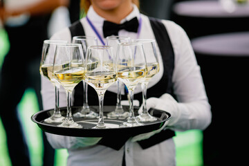 Shallow depth of field (selective focus) details with a waiter walking around and offering glasses of wine to the guests of an event.