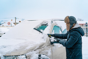 Man clearing snow off the car in a winter day