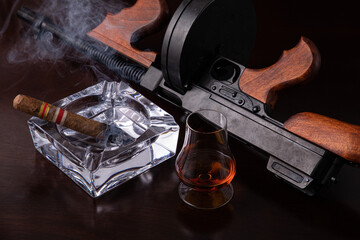 Vintage Thompson submachine gun on a dark brown table with a cigar and whiskey