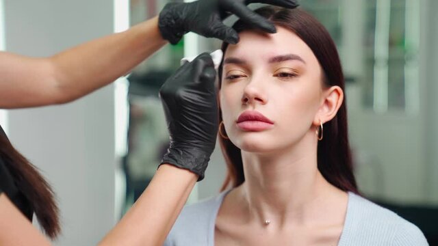 Permanent Makeup Master Prepares a Woman Client for an Eyebrow Microblading Procedure. Beautiful Young Girl in a Spa Salon. Work of a Beautician. Health and Beauty Concept. 
