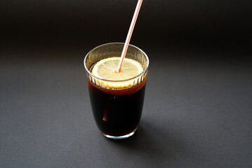Glass of cola with straw, lemon slice and ice cube on black background. Photo taken December 30th, 2021, Zurich, Switzerland.