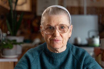 Portrait of an elderly lady in large eyeglasses. At home in the kitchen, looking at the camera.