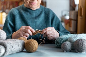 An elderly lady is engaged in an interesting hobby for old people. Knitting at home. Hobbies that you can do without leaving home.