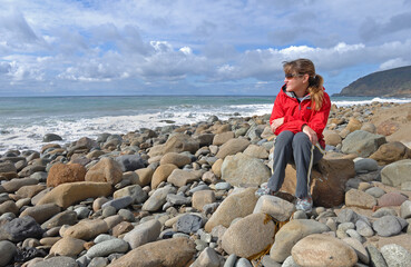 Woman sitting on rocky beach.