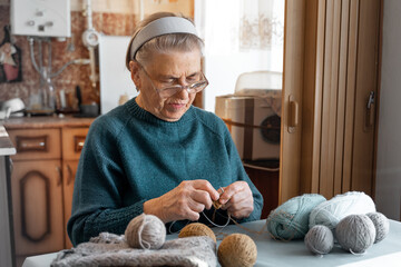 An octogenarian old woman knits with knitting needles using woolen threads. Large glasses for...