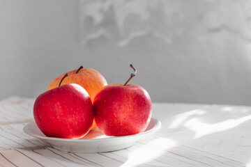 Red apples in a white bowl on a white table in the kitchen.