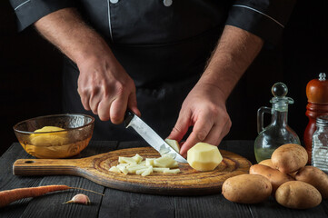 The chef cuts raw potatoes into pieces with a knife before preparing breakfast or dinner. Close-up of a cook hands while working in a restaurant kitchen.