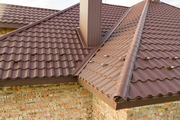 Detail of house roof structure covered with brown metal tile sheets.