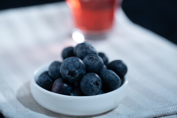 Closeup of a jar of blueberries ona kitchen towel. A glass of blueberry juice in the background.