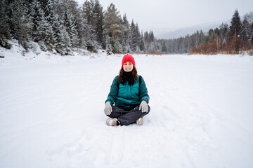 Fototapeta na wymiar A cheerful girl meditates in a snowy valley. a woman sat down to rest in the snow. A walk in the forest in winter, filled with peace, tranquility and joy