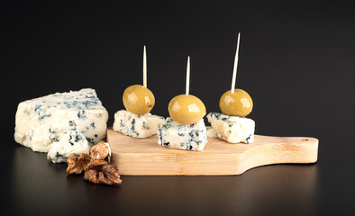 Cheese with blue mold and large green olives on a wooden cutting board, isolated on a black...