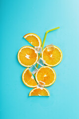 A composition of orange slices and ice cubes with a straw on a blue background in the form of a refreshing drink